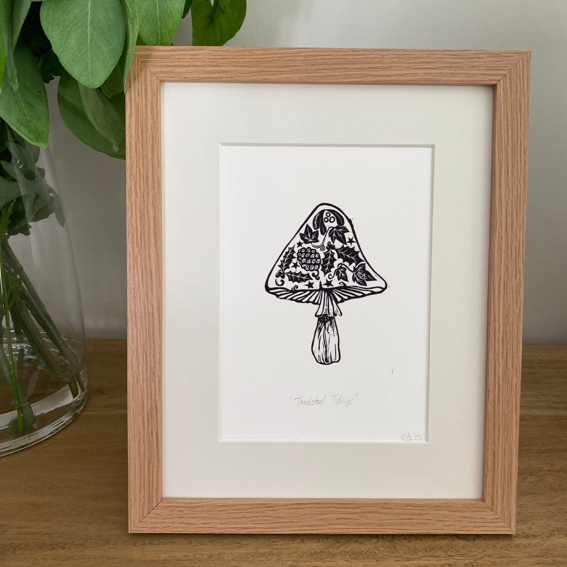 Framed black and white illustration of a mushroom on a wooden surface with a plant in the background.