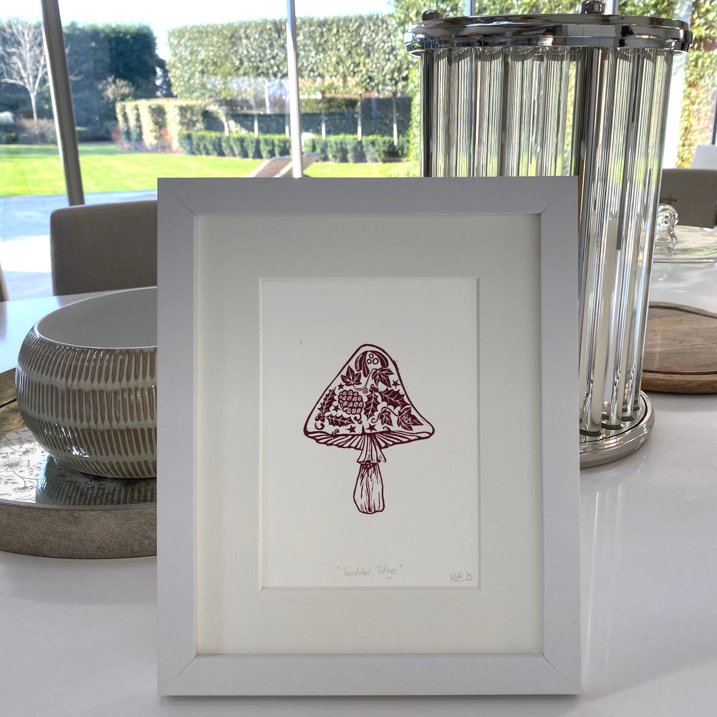 Framed artwork of a mushroom on a table with decorative elements.