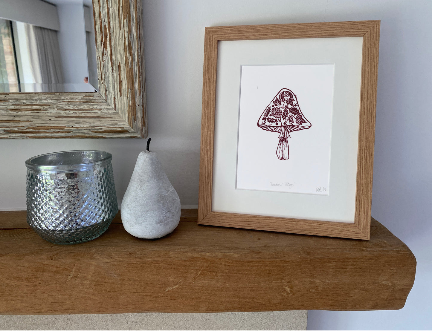 Framed artwork of a mushroom on a wooden shelf with a pear and candle.