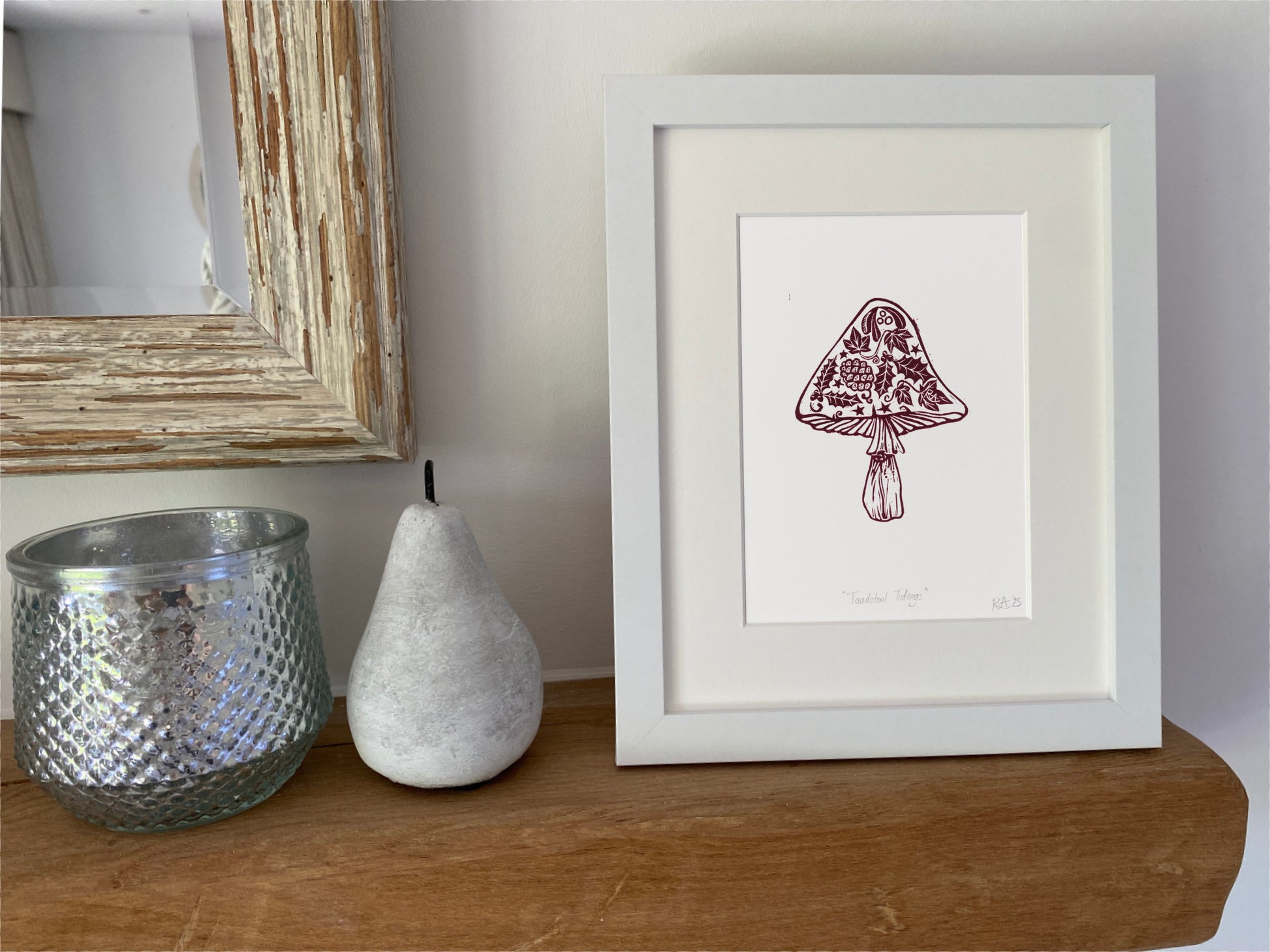 Framed artwork of a mushroom on a wooden surface with decorative items.