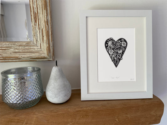 Framed artwork of a black tudor heart with floral patterns on a wooden surface with decorative items.