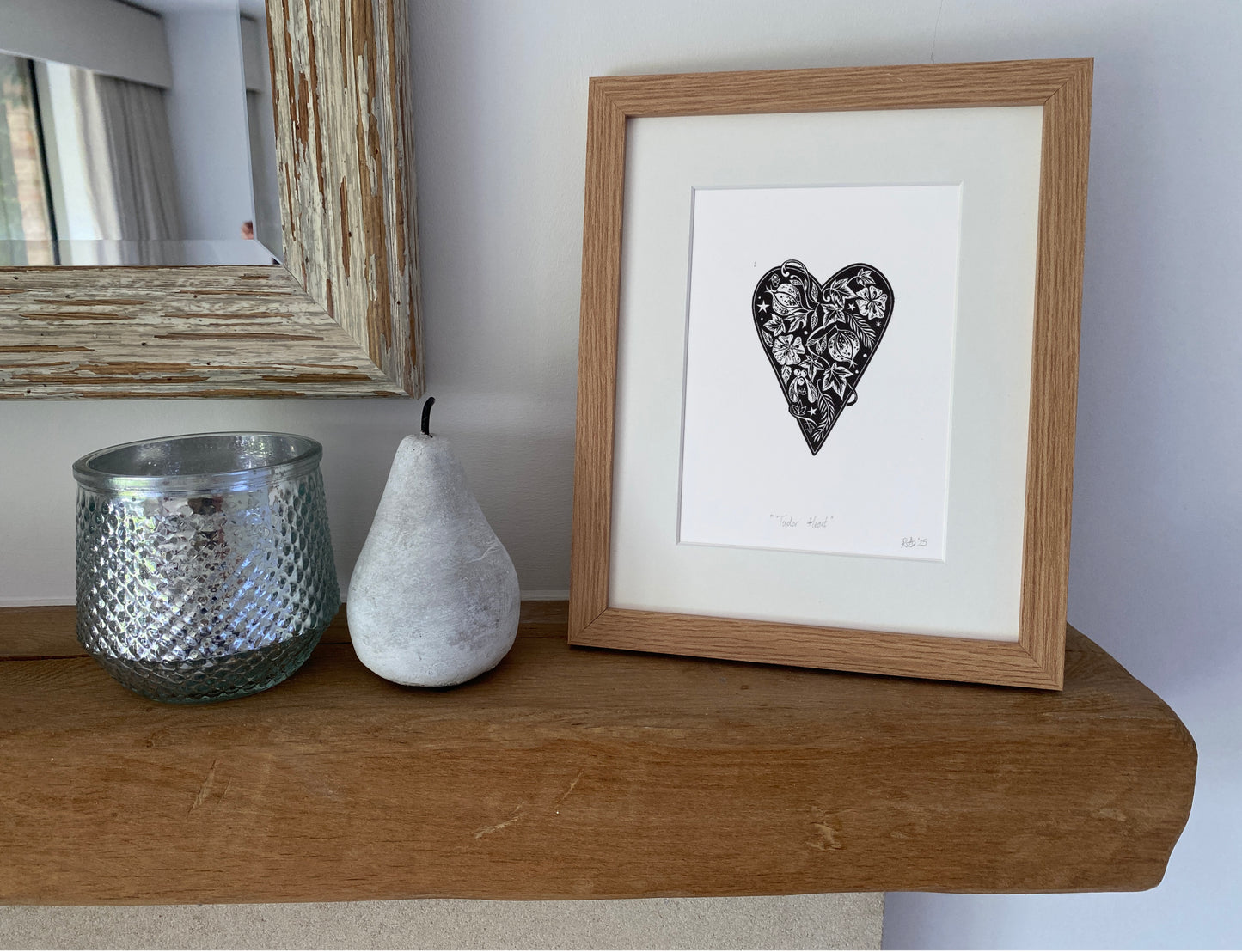 Framed artwork of a black heart with white center on a wooden shelf with decorative items.