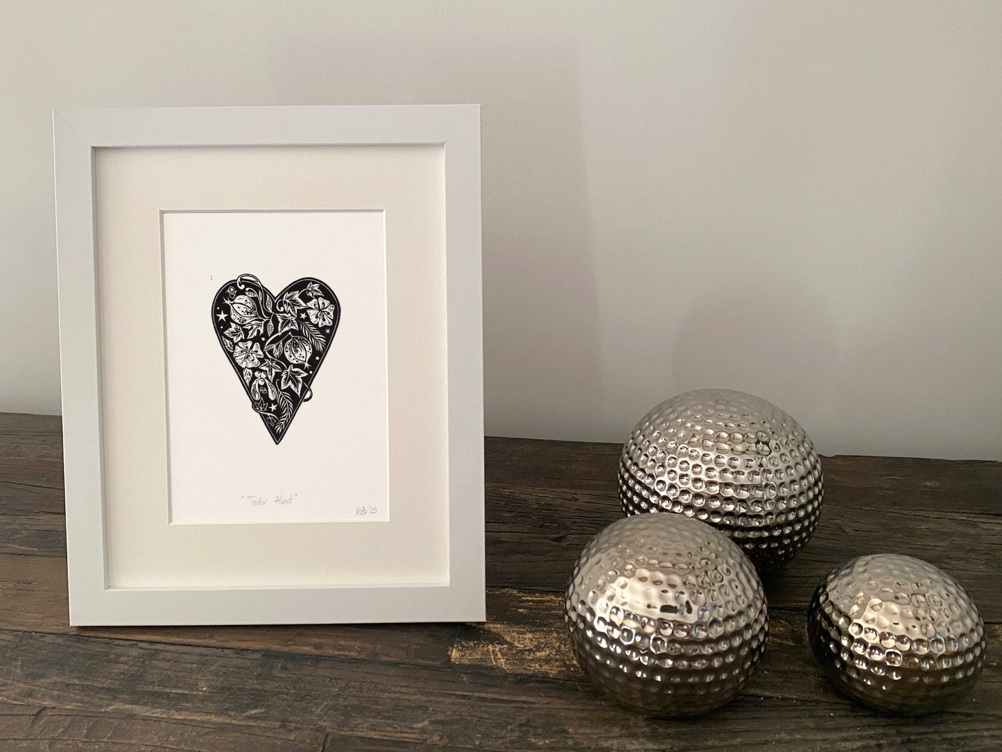Framed artwork with a heart design on a wooden surface with decorative metallic balls.