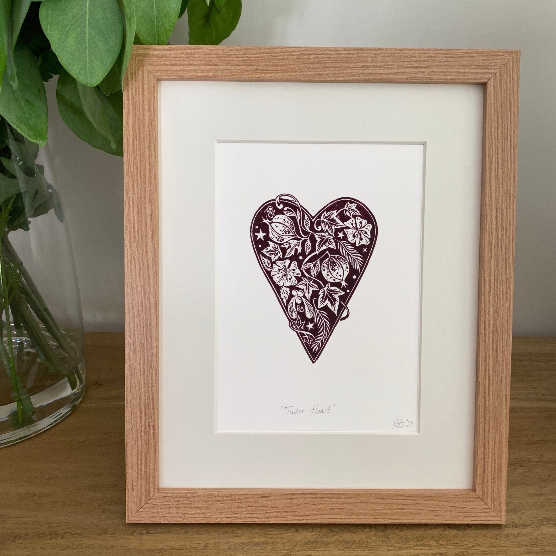 Framed artwork of a heart design on a white background, next to a plant.