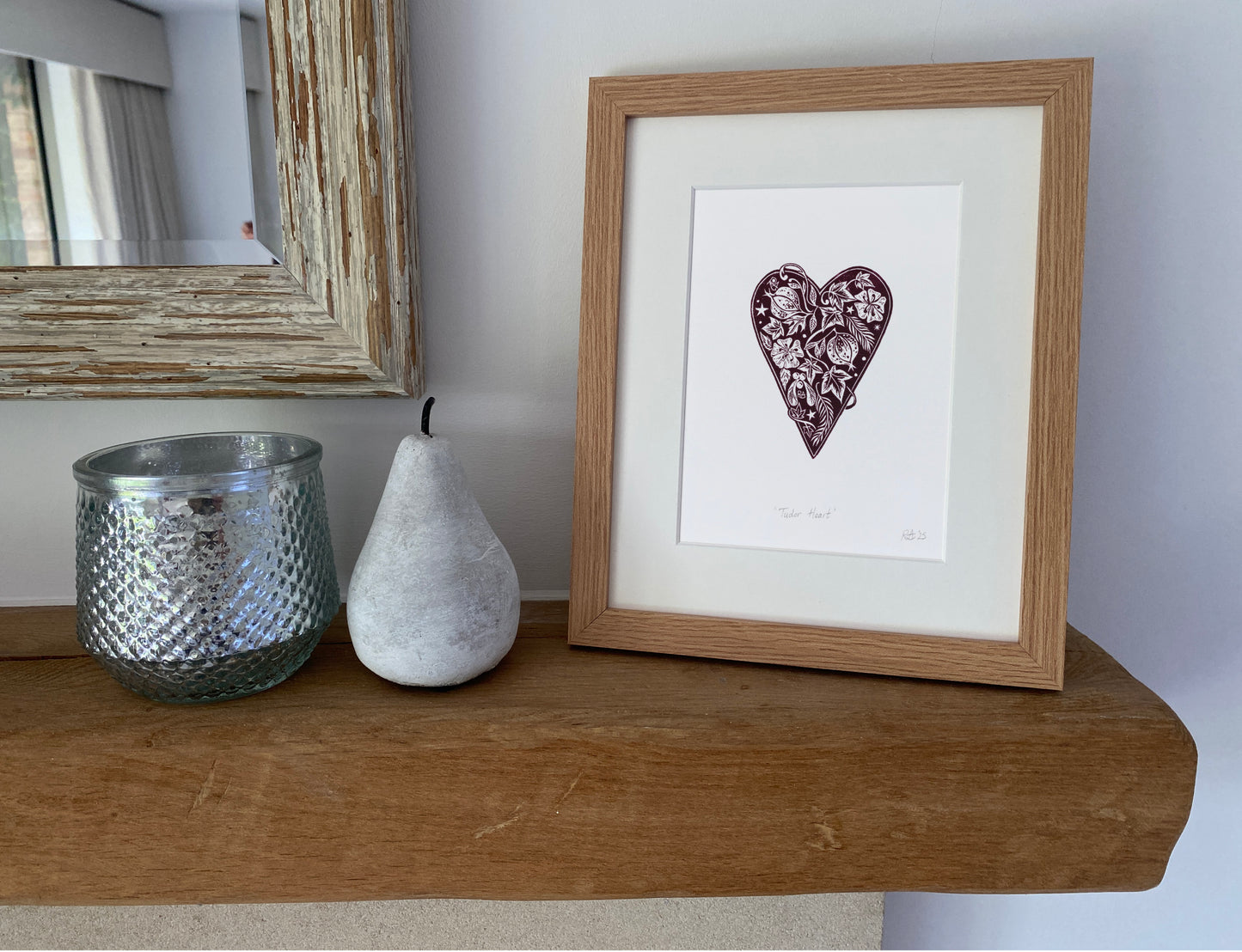 Framed artwork of a heart with floral patterns on a wooden shelf with decorative items.