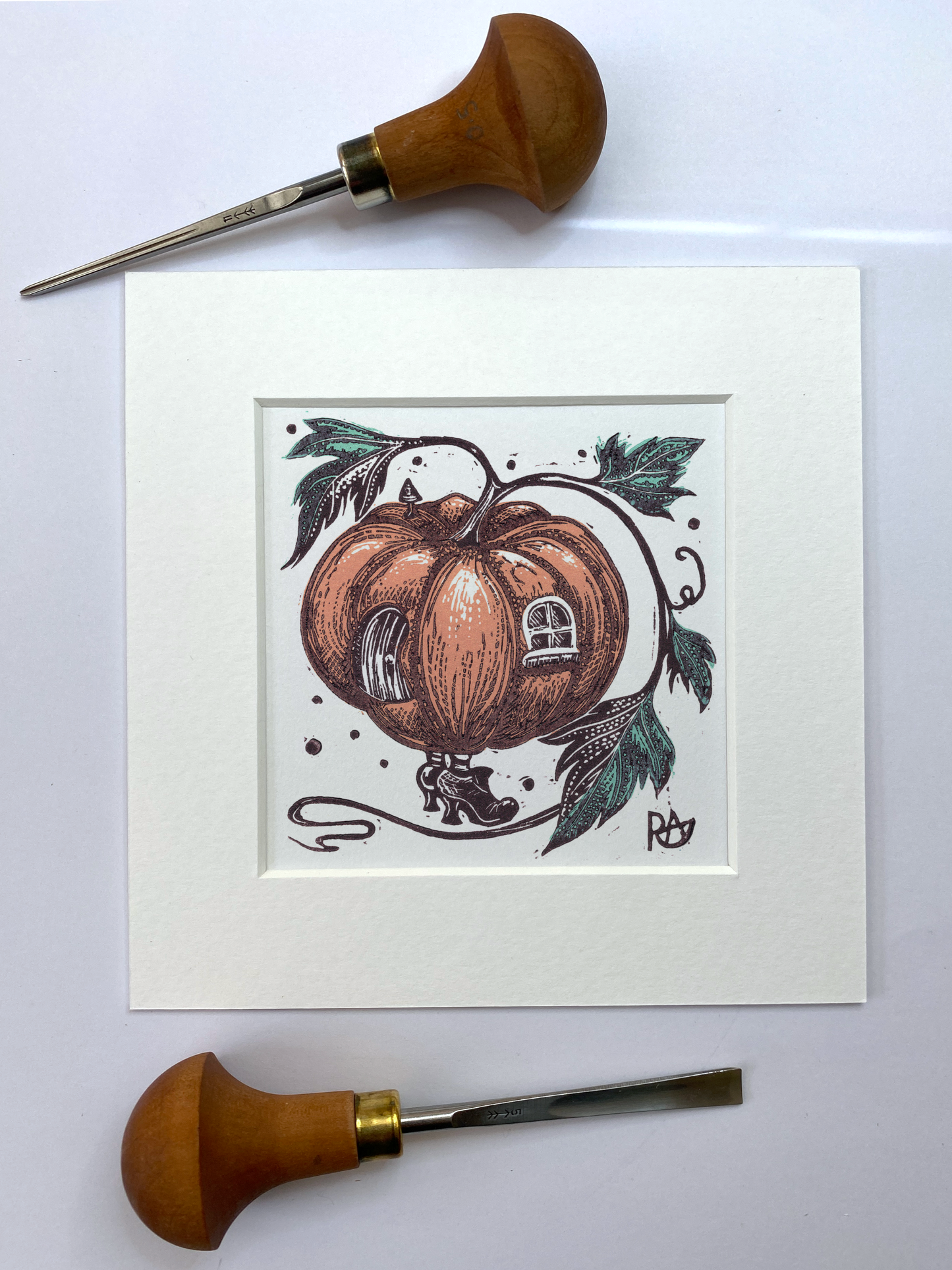 Wooden carving tools and a framed illustration of a pumpkin with decorative elements on a white background