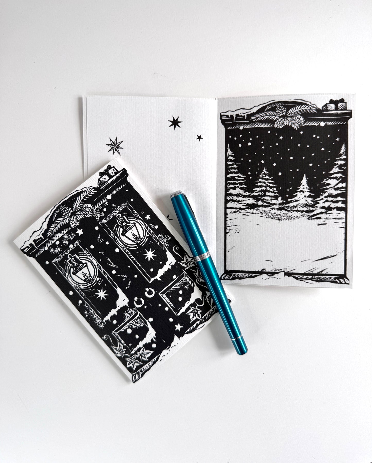 A styled flat-lay of black and white handprinted card on a white background, including a card with a snowy night scene, a matching inside print.