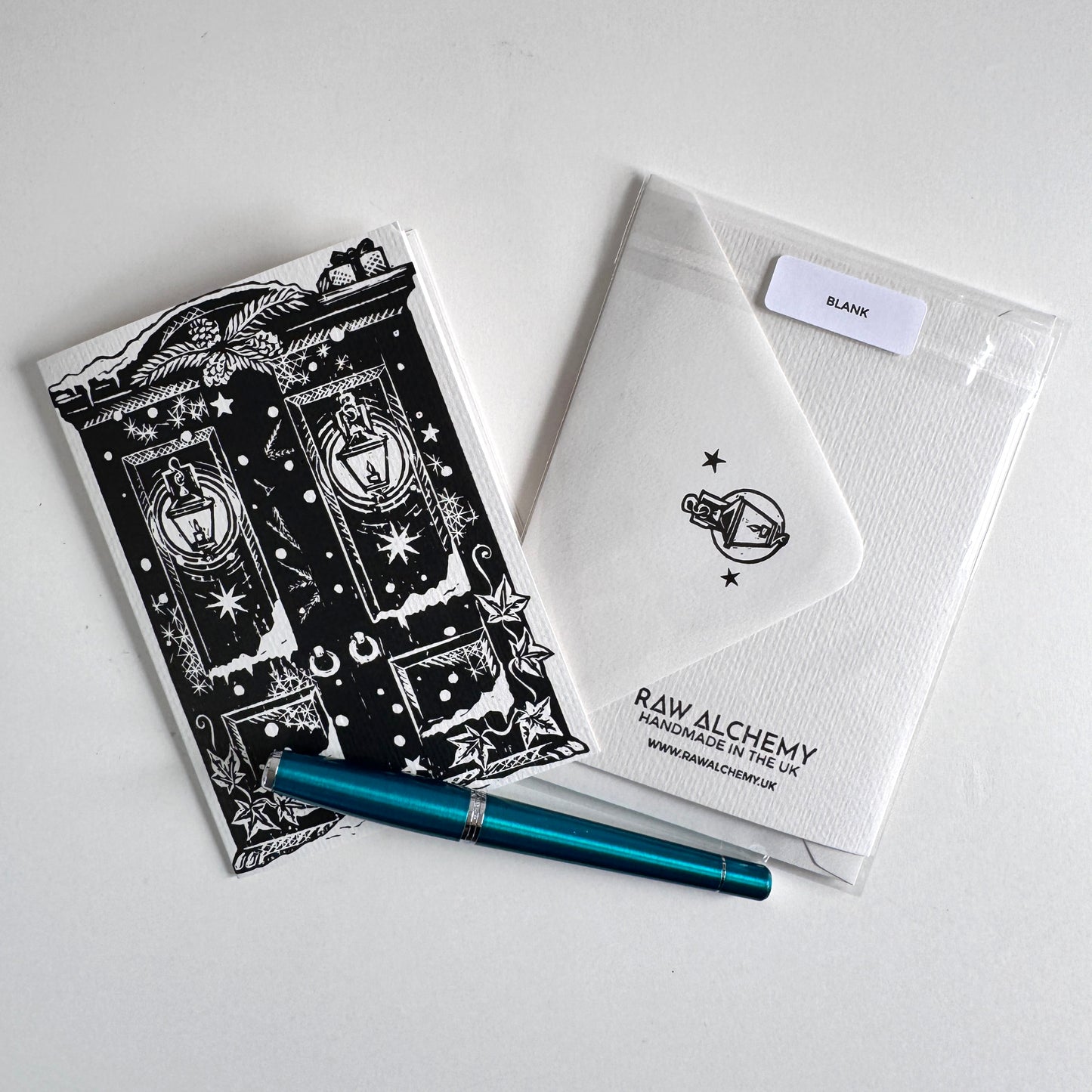 A flat-lay of a stationery set on a light gray surface, featuring a black and white hadprinted card, a white textured envelope with a logo.