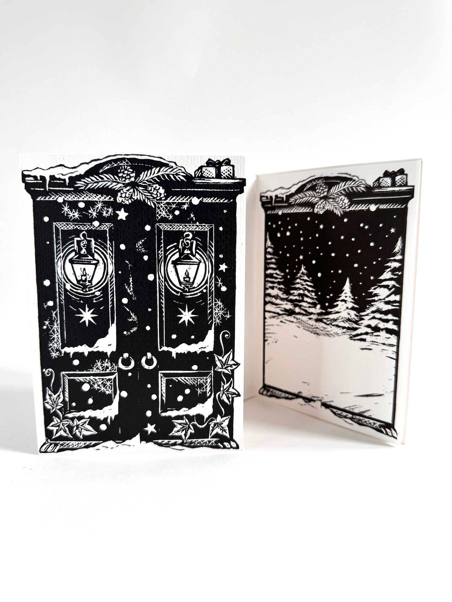 A black and white hand printed linoprint art card featuring a Christmas wardrobe with lanterns and stars, shown with one flat front view and one folded back view displaying a snowy night scene.