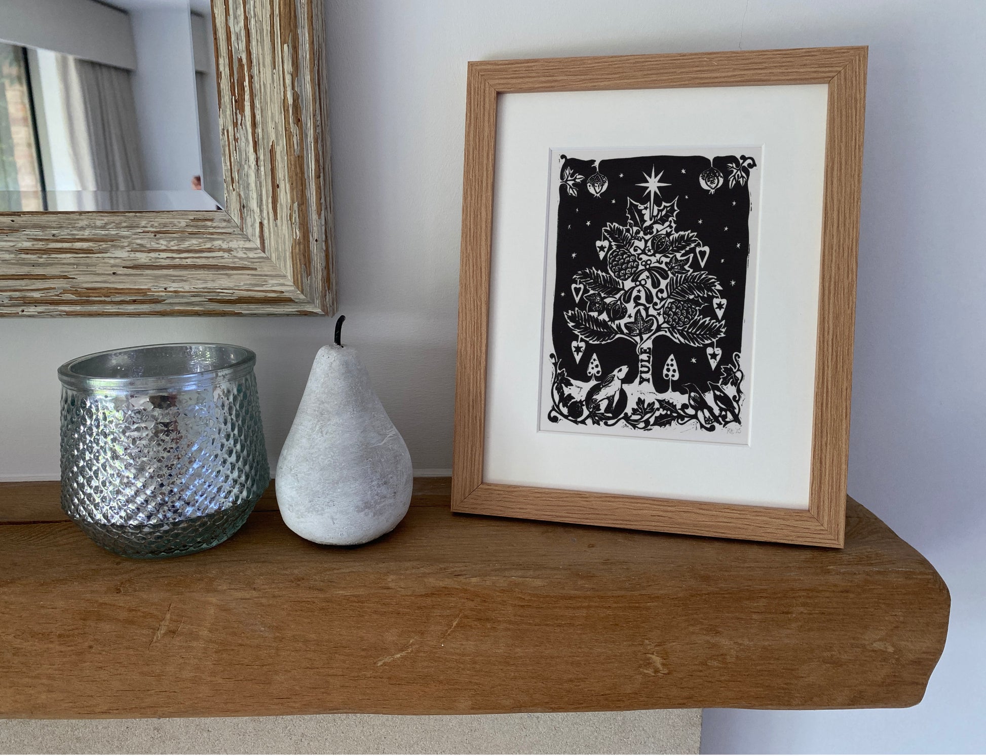 Framed black and white artwork on a wooden shelf with a pear and candle.